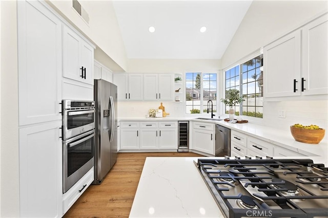 kitchen featuring visible vents, wine cooler, a sink, appliances with stainless steel finishes, and vaulted ceiling
