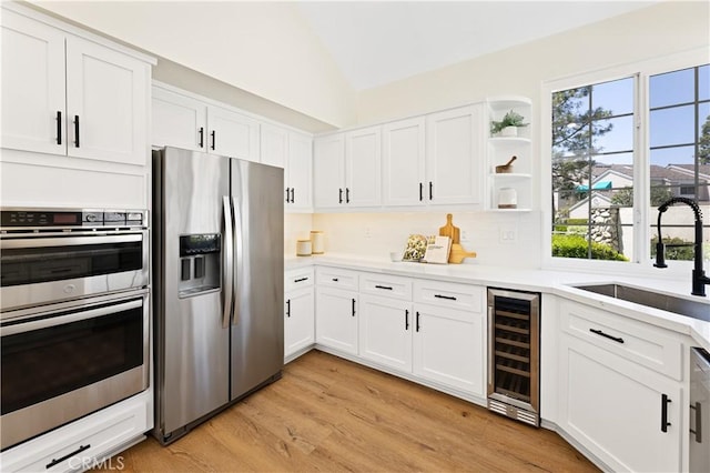 kitchen featuring vaulted ceiling, a sink, wine cooler, stainless steel appliances, and white cabinetry