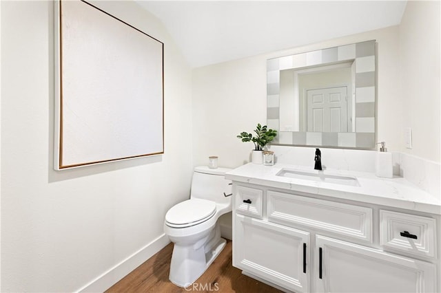 half bath with wood finished floors, vanity, baseboards, toilet, and lofted ceiling