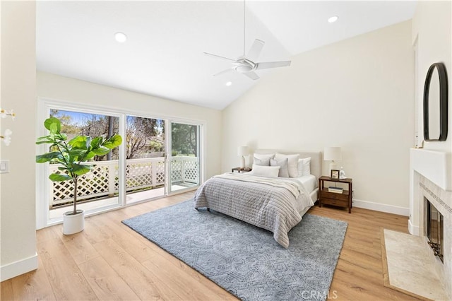 bedroom featuring access to outside, baseboards, a fireplace with flush hearth, light wood-type flooring, and vaulted ceiling