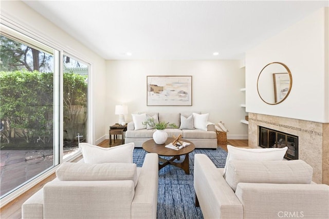 living room featuring a high end fireplace, baseboards, built in features, and wood finished floors