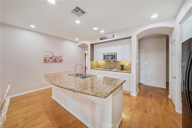 kitchen with gas cooktop, a sink, arched walkways, stainless steel microwave, and visible vents