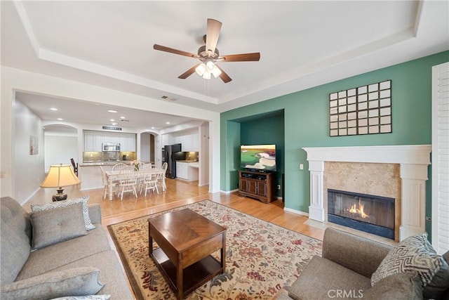living room featuring arched walkways, a tray ceiling, ceiling fan, and light wood-type flooring