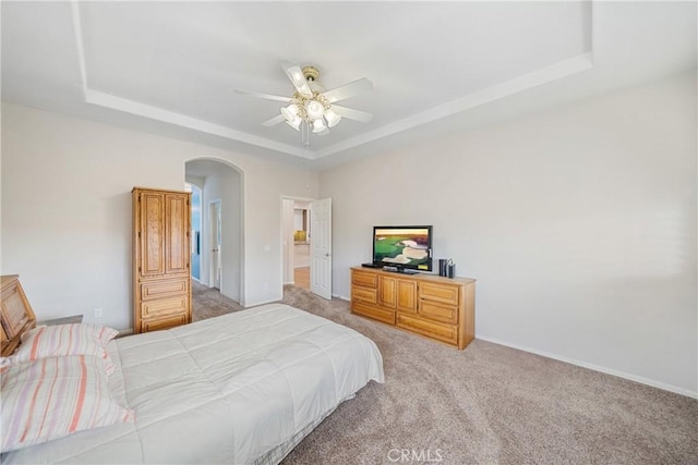 bedroom featuring light colored carpet, arched walkways, and a tray ceiling