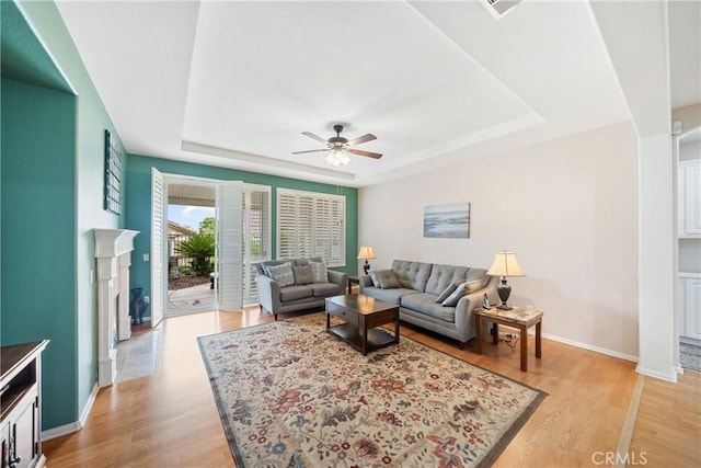 living room with a ceiling fan, a tray ceiling, and light wood-style floors