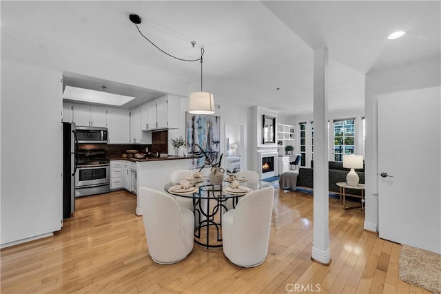dining room with recessed lighting, light wood-style flooring, and a lit fireplace