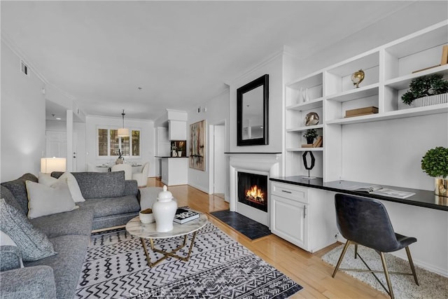 living room with crown molding, visible vents, baseboards, a lit fireplace, and light wood-type flooring