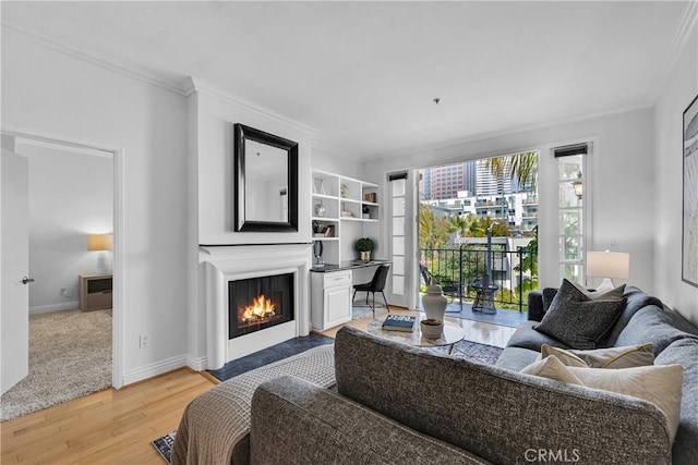 living area featuring baseboards, ornamental molding, light wood finished floors, and a fireplace with flush hearth