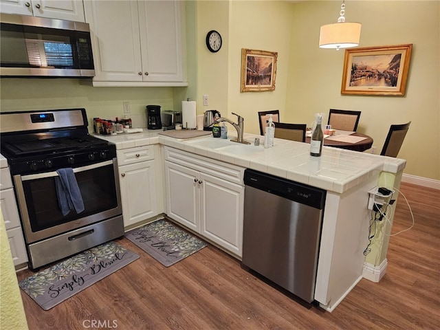 13435 Cascade Ct, Cerritos, CA 90703 - kitchen with a peninsula, wood finished floors, a sink, white cabinets, and appliances with stainless steel finishes