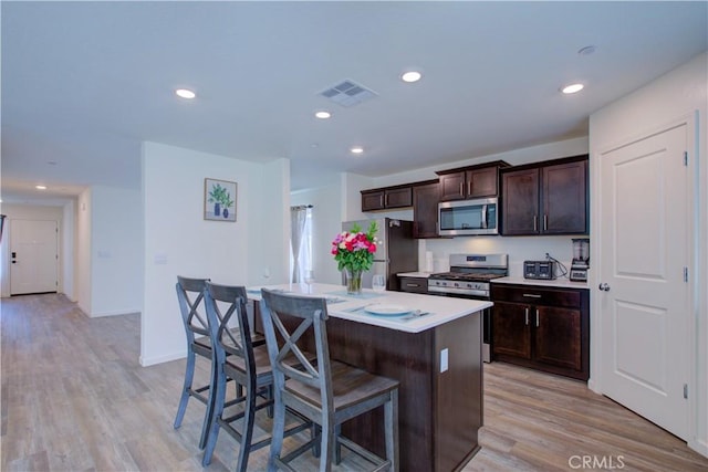 218 Bryce Canyon Ct, Merced, CA 95341 - kitchen featuring appliances with stainless steel finishes, a kitchen bar, dark brown cabinets, a kitchen island, and light wood-type flooring