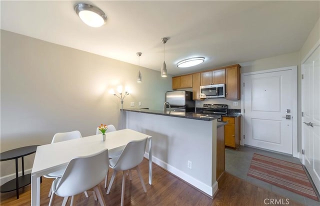 10982 Roebling Ave Unit 367, Los Angeles, CA 90024 - kitchen featuring appliances with stainless steel finishes, dark countertops, wood finished floors, pendant lighting, and a peninsula