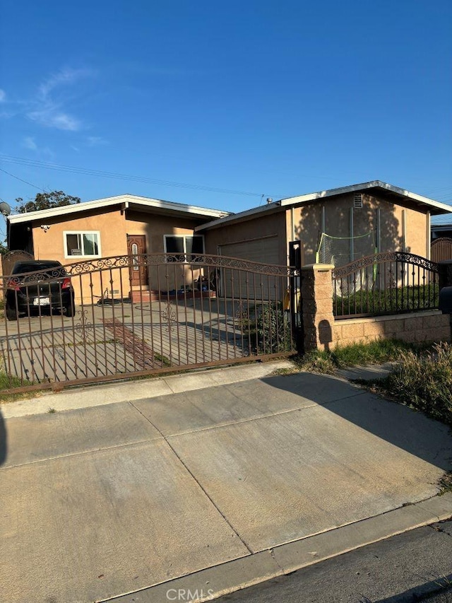 view of front of property featuring a garage, stucco siding, a gate, a fenced front yard, and driveway