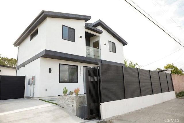 contemporary home with a gate, a fenced front yard, a balcony, and stucco siding