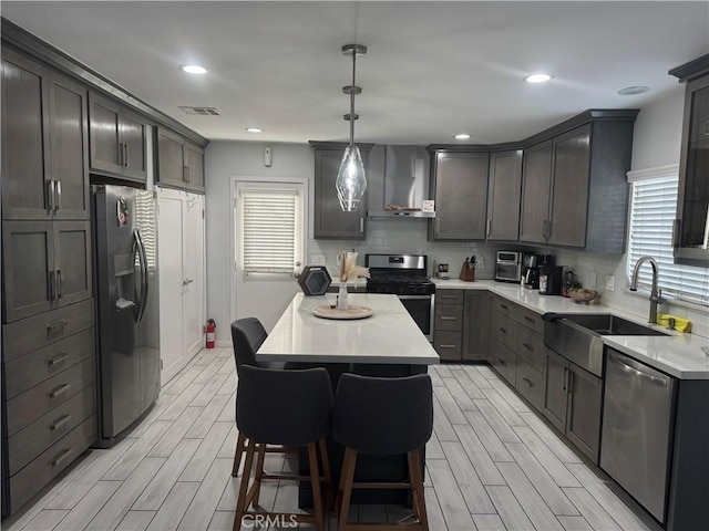 kitchen with wall chimney range hood, wood finish floors, appliances with stainless steel finishes, and a sink
