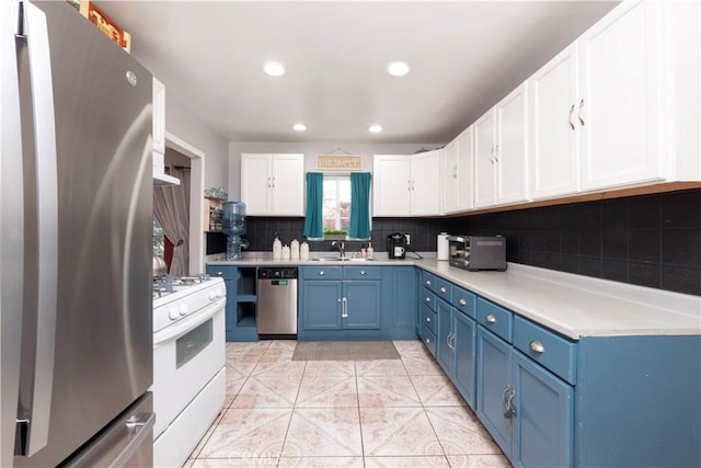kitchen with appliances with stainless steel finishes, a sink, blue cabinetry, white cabinetry, and tasteful backsplash
