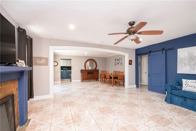 living room with a brick fireplace, baseboards, recessed lighting, a barn door, and a ceiling fan