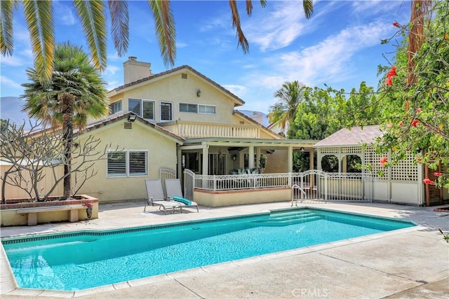 rear view of property with a chimney, fence, an outdoor pool, a patio area, and stucco siding