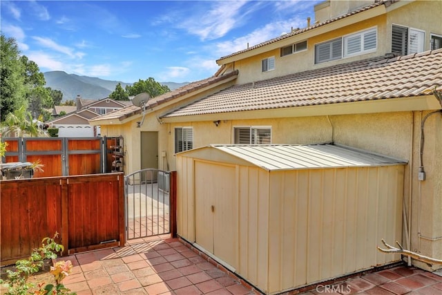 back of property featuring a mountain view, fence, an outdoor structure, a shed, and a gate