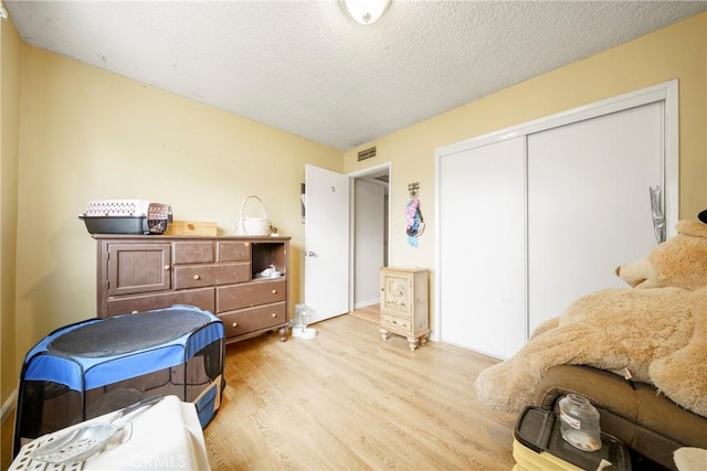bedroom featuring a closet, light wood-type flooring, a textured ceiling, and visible vents