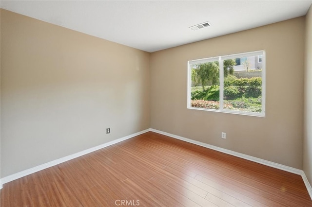 unfurnished room with baseboards, wood finished floors, and visible vents