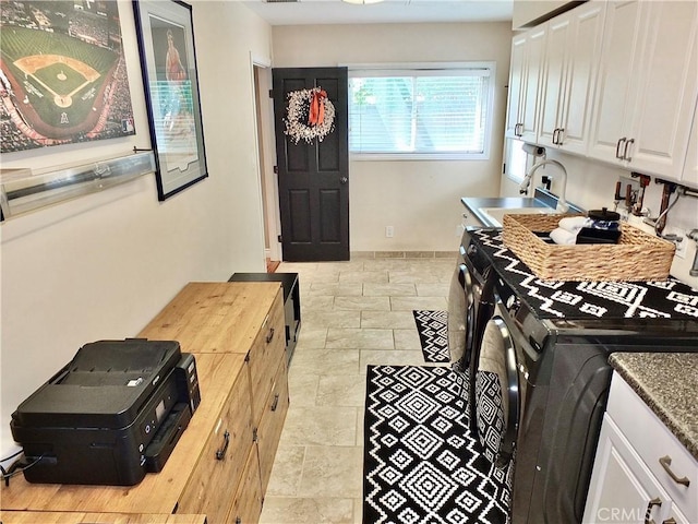 washroom with a sink, washing machine and clothes dryer, cabinet space, and stone tile floors