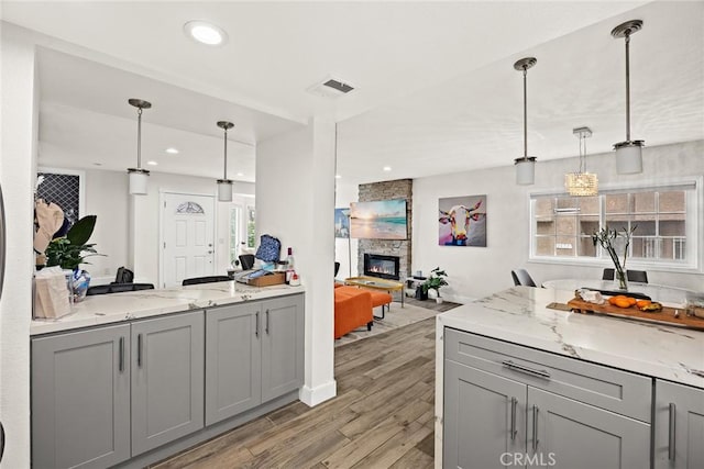 kitchen with light wood-style floors, open floor plan, a stone fireplace, and gray cabinetry