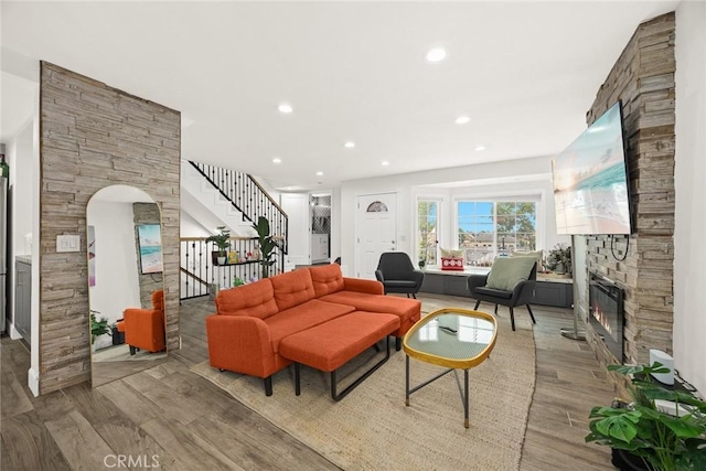 living area with a fireplace, arched walkways, recessed lighting, wood finished floors, and stairway