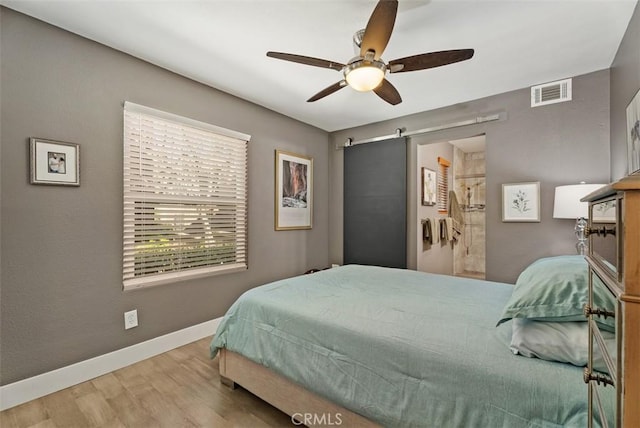 bedroom featuring a ceiling fan, visible vents, a barn door, wood finished floors, and baseboards