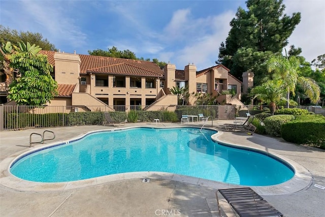 community pool with a patio area, fence, and a residential view
