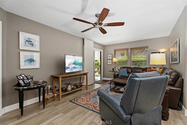 living room featuring baseboards, a ceiling fan, and light wood finished floors