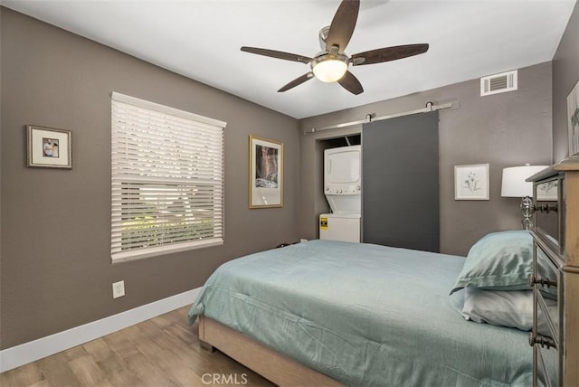 bedroom featuring visible vents, wood finished floors, stacked washer / dryer, baseboards, and a ceiling fan