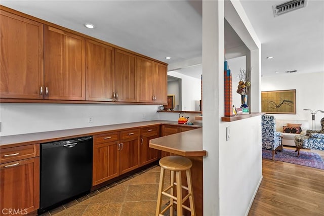 kitchen with a breakfast bar area, black dishwasher, brown cabinets, and visible vents