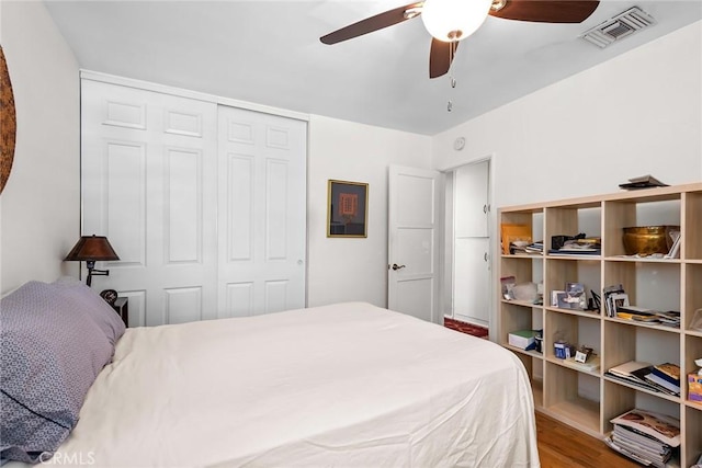 bedroom with ceiling fan, visible vents, wood finished floors, and a closet