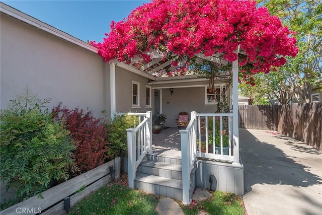 view of exterior entry featuring a porch, fence, and stucco siding