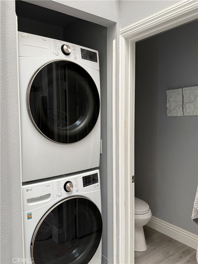 laundry room featuring baseboards, stacked washer / drying machine, wood finished floors, and laundry area