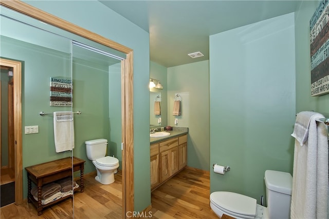 bathroom with vanity, toilet, wood finished floors, and visible vents