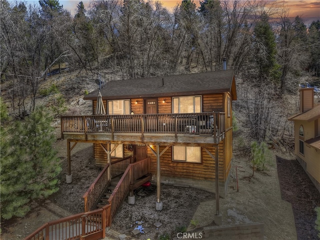 back of property at dusk with roof with shingles, a wooden deck, and stairway