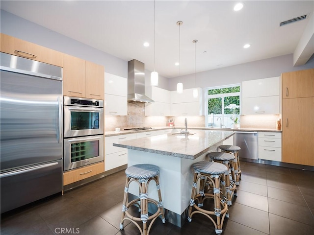 kitchen featuring modern cabinets, wall chimney range hood, visible vents, and appliances with stainless steel finishes