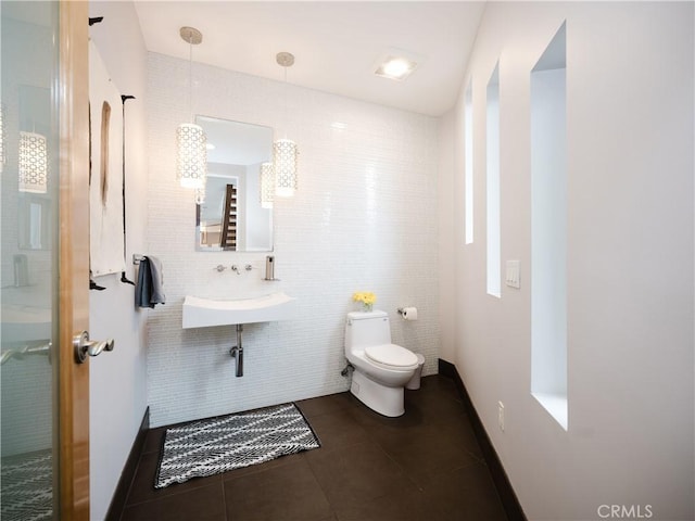 bathroom featuring toilet, tile walls, tile patterned floors, and a sink