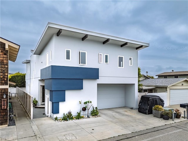 contemporary house featuring concrete driveway, a garage, stucco siding, and fence