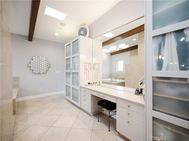 bathroom featuring baseboards, beamed ceiling, tile patterned floors, and a skylight
