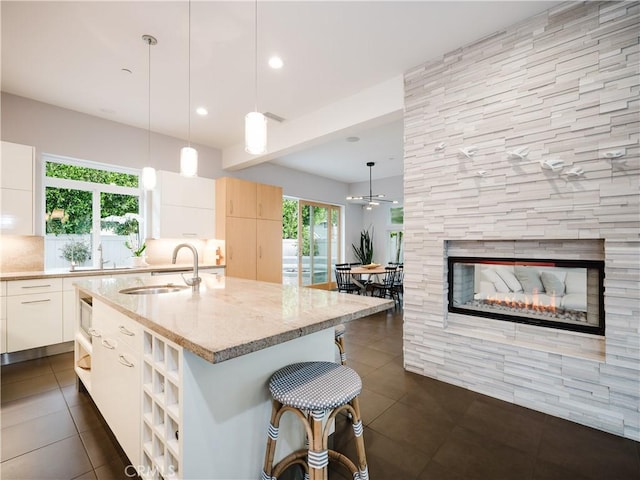 kitchen featuring light stone countertops, a sink, dark tile patterned floors, a kitchen breakfast bar, and a center island with sink