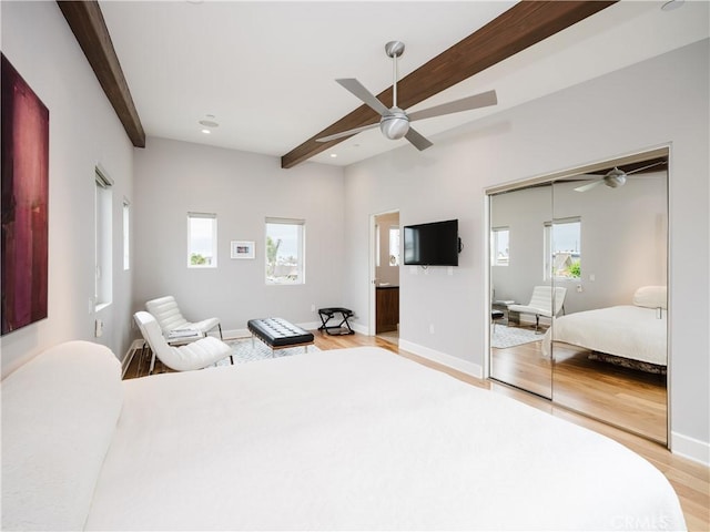 bedroom with beamed ceiling, light wood-style floors, a closet, and multiple windows