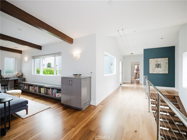 interior space featuring light wood finished floors, baseboards, and vaulted ceiling with beams