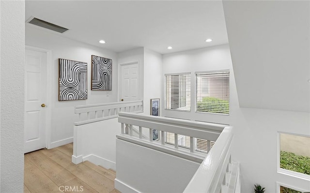 hall featuring light wood-style floors, plenty of natural light, visible vents, and an upstairs landing