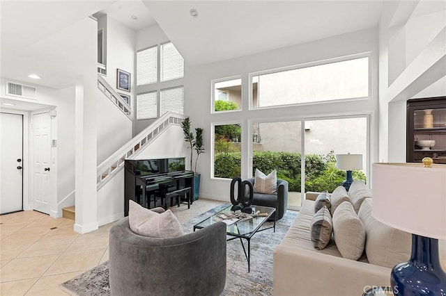 living area with visible vents, a towering ceiling, light tile patterned floors, and stairway