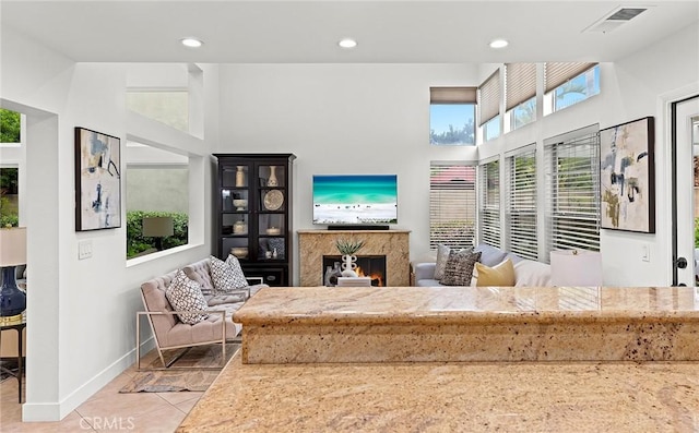 tiled living area with baseboards, visible vents, a high ceiling, and a premium fireplace