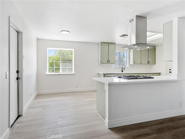 kitchen with gas cooktop, a wealth of natural light, green cabinetry, and island range hood