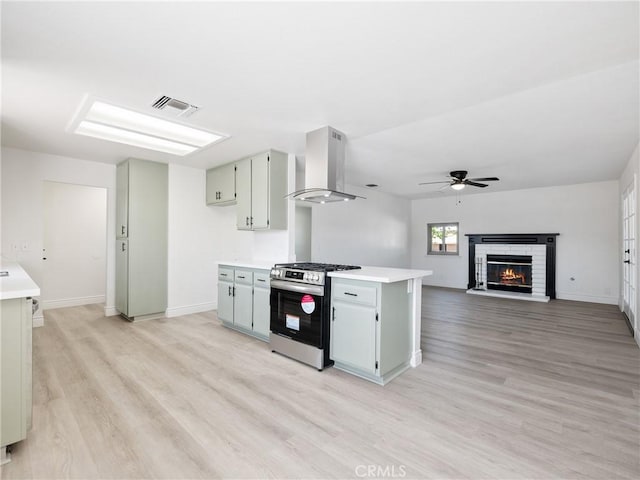 kitchen with visible vents, stainless steel range with gas stovetop, light wood-type flooring, light countertops, and ventilation hood