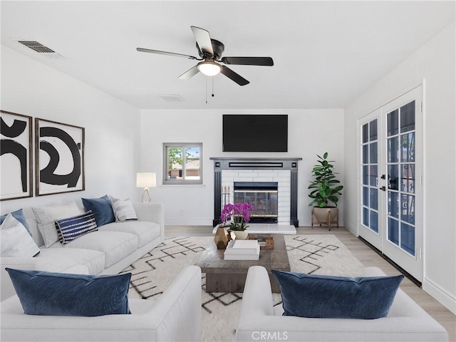 living room featuring a ceiling fan, french doors, visible vents, a brick fireplace, and light wood finished floors